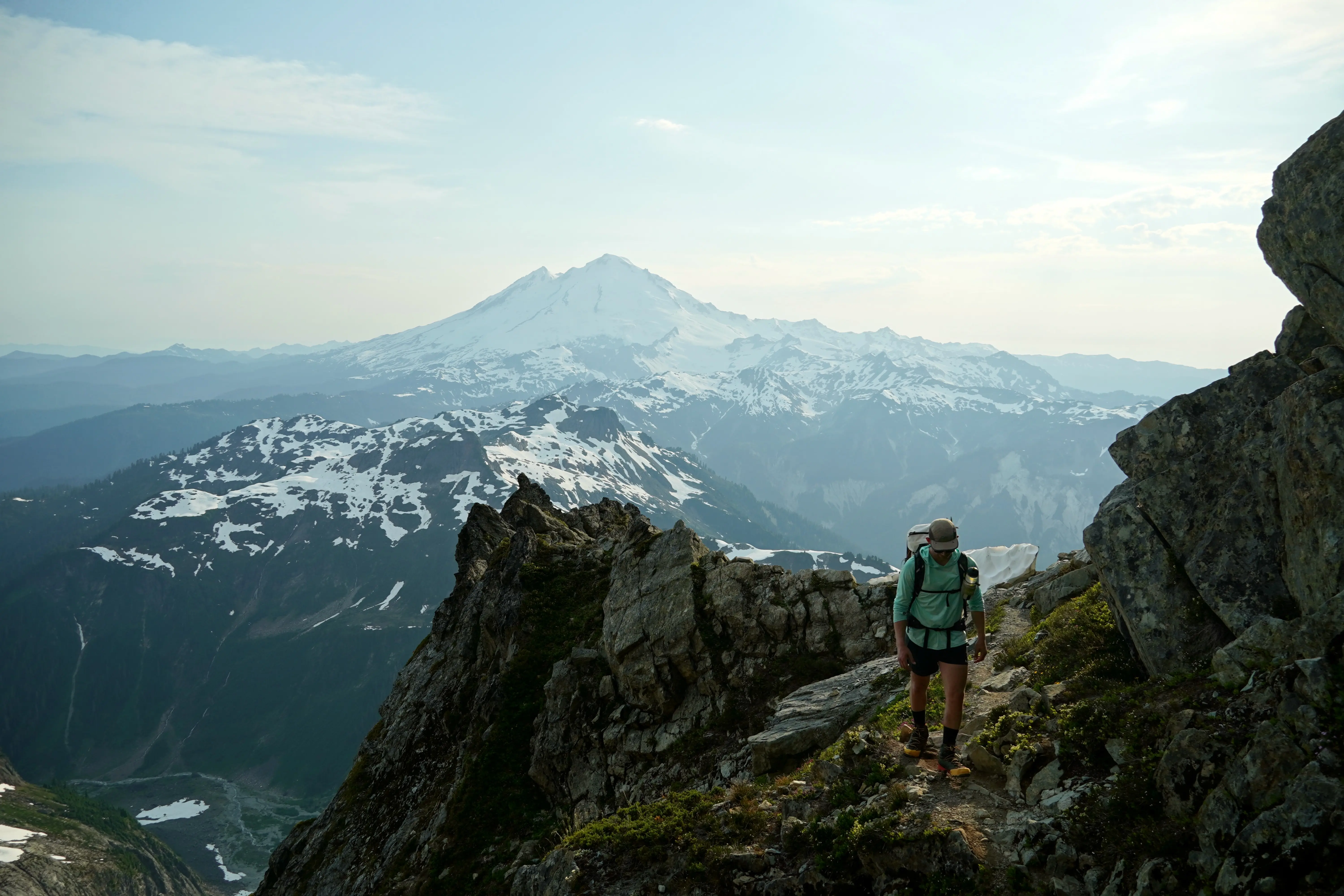 Cooper Stewart on Fisher's Chimney, Mt Shuksan with Mt. Baker in the background. Photo credit: Shane Haynes